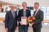 Überreichung Urkunde und Blumen drei Männer